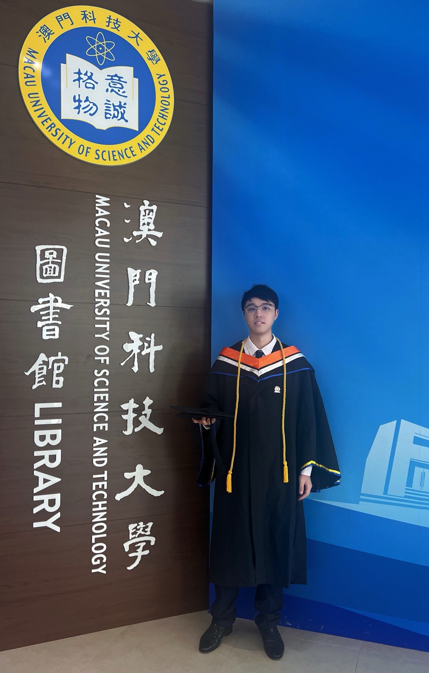 Boyi Fu in graduation attire at the M.U.S.T. library